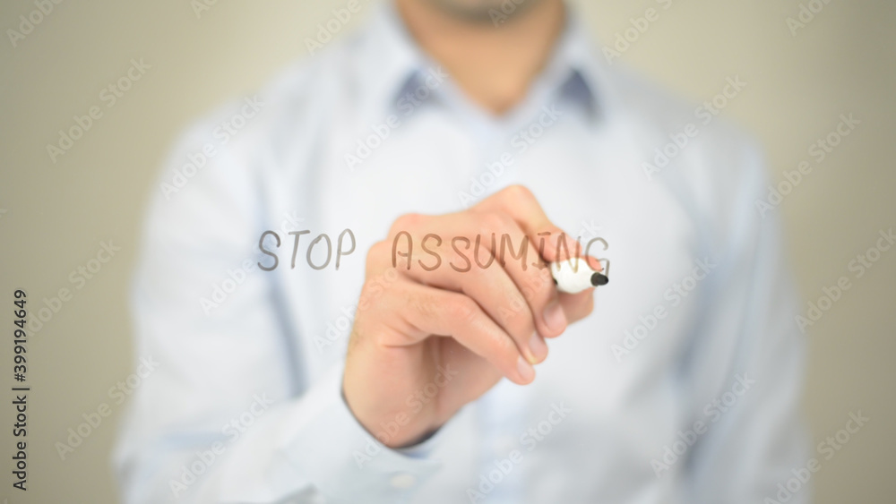 Stop Assuming , man writing on transparent screen Stop Assuming , man writing on transparent screen
