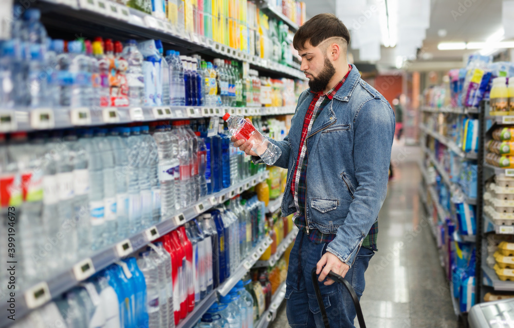 Portrait of focused young glad cheerful positive smiling man purchasing bottled water in grocery store