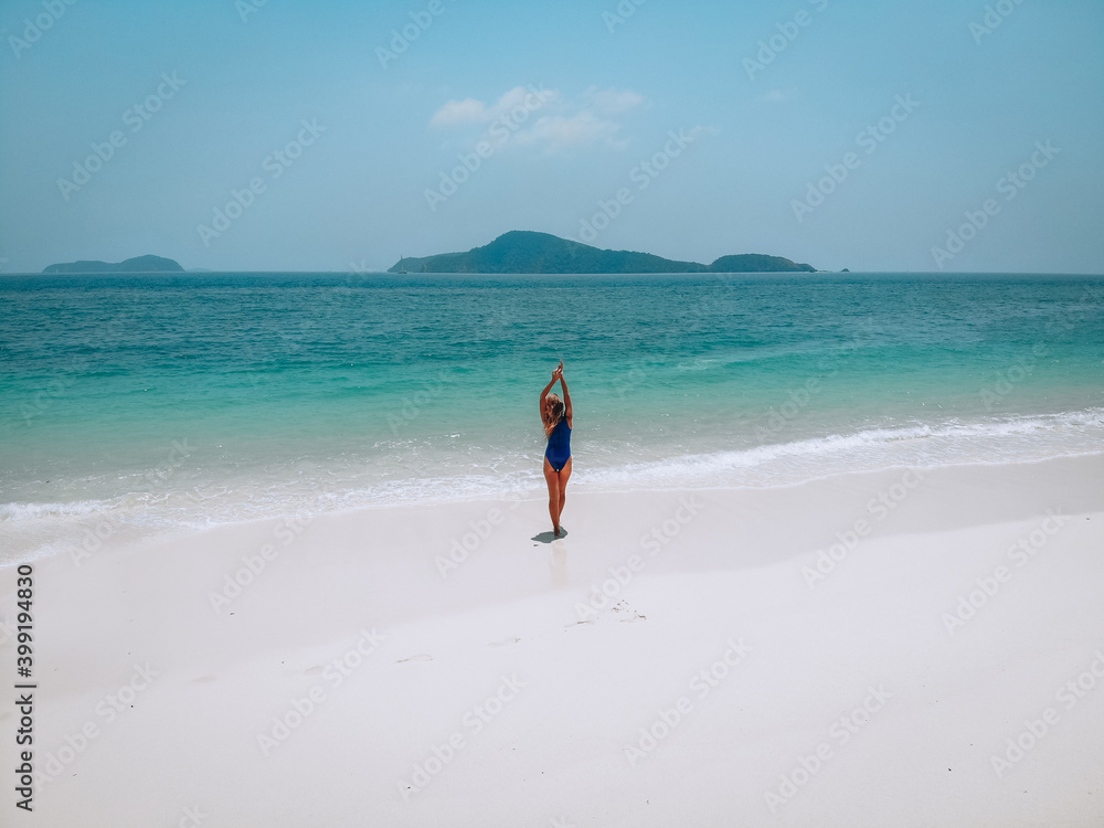 Young attractive woman in a blue swimming suit standing on a sandy beach and sunbathing. Summer vacation concept