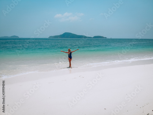 Young attractive woman in a blue swimming suit standing on a sandy beach and sunbathing. Summer vacation concept