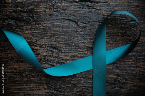 Top view of  teal ribbon on dark background with copy space. Cervical and ovarian cancer, sexual assault, pcos, ptsd, anxiety disorder, agoraphobia and scleroderma awareness concept. photo