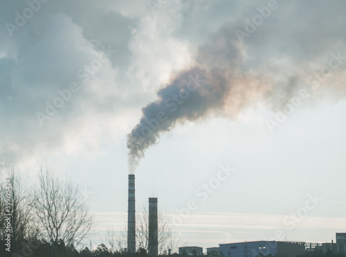 Smoke from chimneys at the plant in the rays of the sunset as a background.
