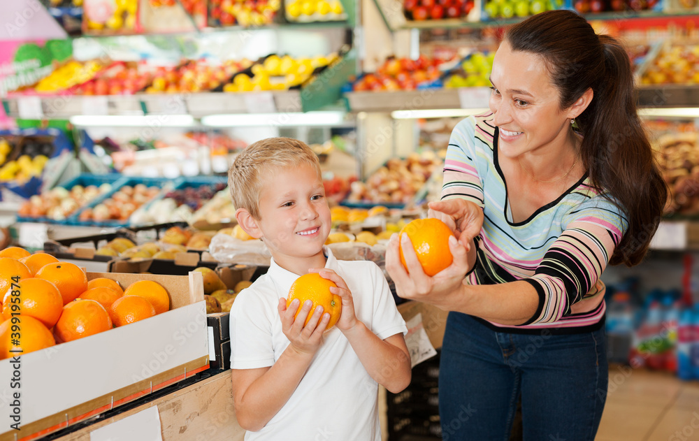 Fototapeta premium portrait of young mother with little boy buying oranges at store