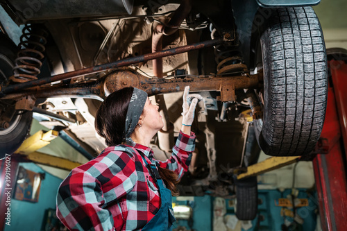 Portrait of a young woman mechanic conducting an inspection of the car body. Side view. Bottom view