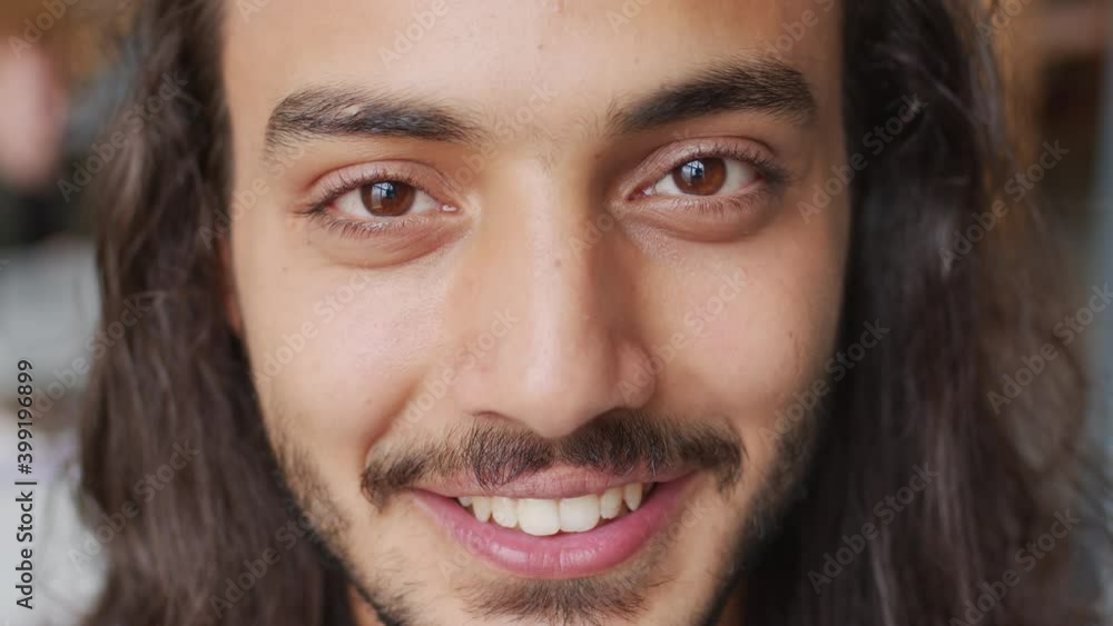 Extreme close up of handsome young Arab man with long hair and beard looking at camera and smiling Extreme close up of handsome young Arab man with long hair and beard looking at camera and smiling