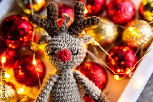 Handmade crocheted deer on the background of Christmas balls and garland lights. © nadezhda