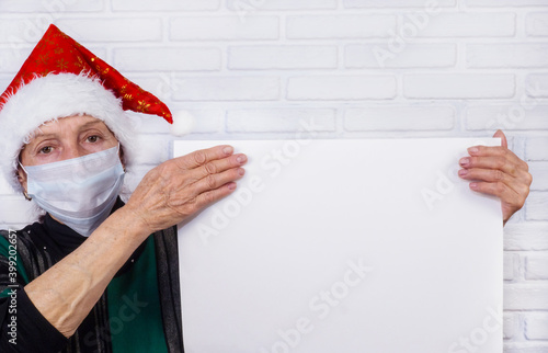 Covid-19. An old woman in a medical disposable mask holds a white sheet with wrinkled hands. An elderly pensioner. Retirement age concept. Christmas. background and texture.