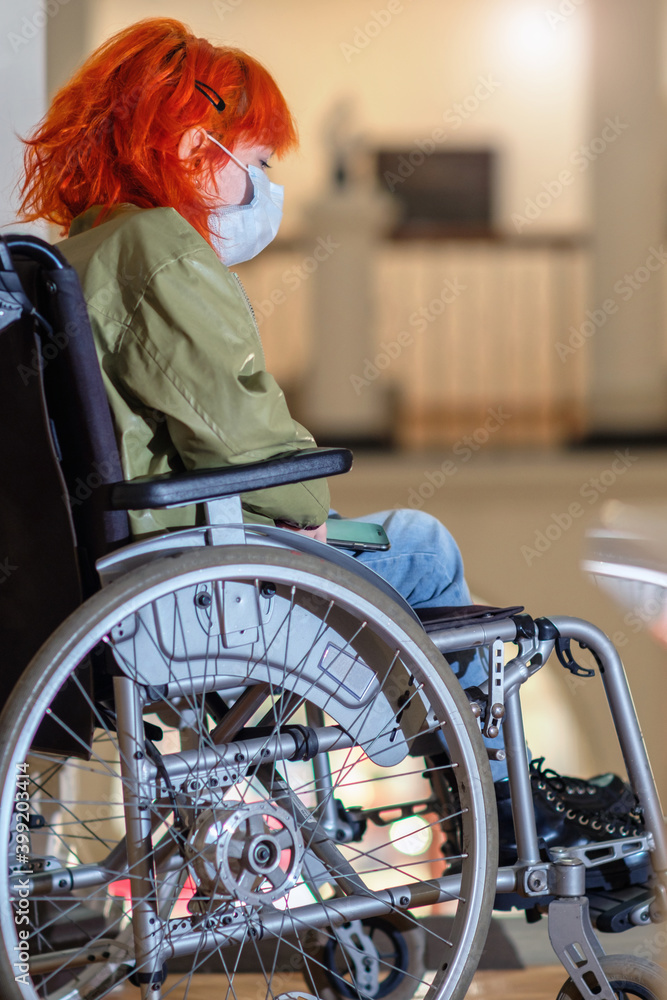 Disabled girl with red hair in a wheelchair visiting the art gallery, selective focus