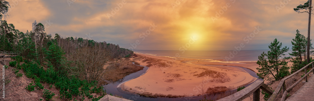 Panorama view of white sand beach and sunset over Baltic sea surrounded by conifer trees forest in Latvia. The White Dune and Baltic see at Saulkrasti in autumn. Sunset panorama. Panorama view of white sand beach and sunset over Baltic sea surrounded by conifer trees forest in Latvia. The White Dune and Baltic see at Saulkrasti in autumn. Sunset panorama.