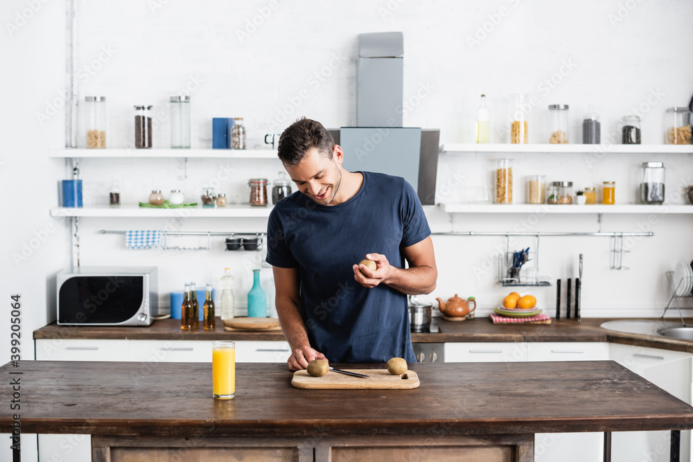 man looking at kiwi on cutting board near orange juice in glass on table in kitchen man looking at kiwi on cutting board near orange juice in glass on table in kitchen