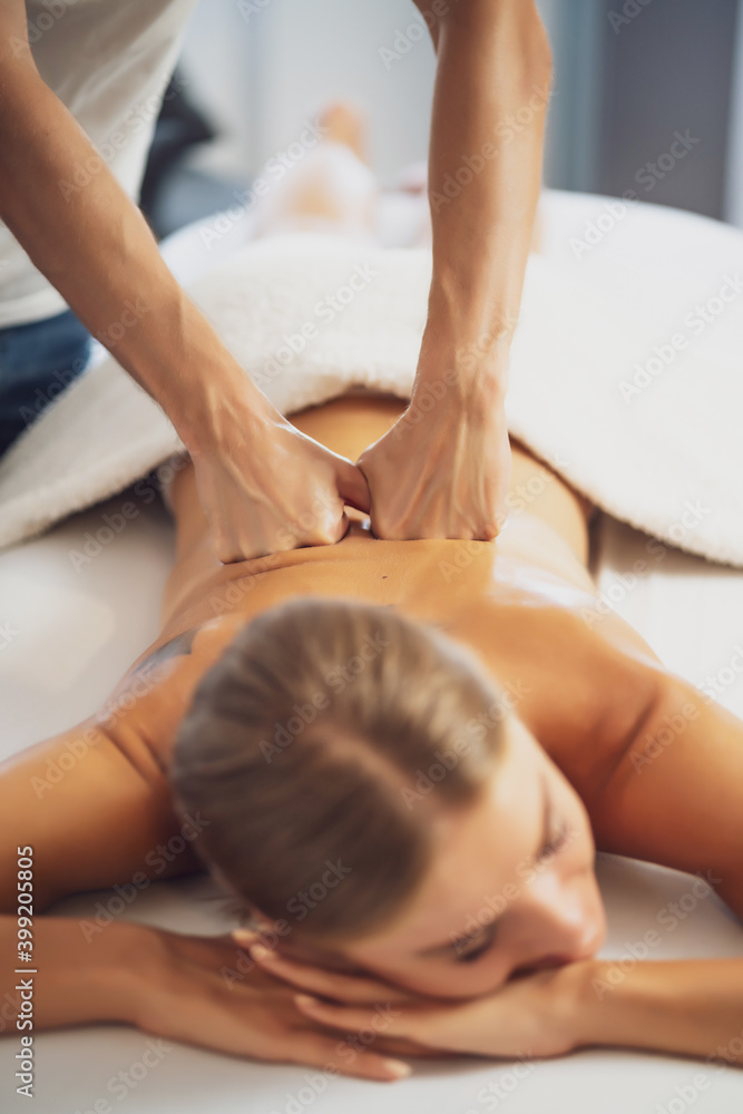 Professional masseur doing therapeutic massage. Woman enjoying massage in her home. Young woman getting relaxing body massage. - obrazy, fototapety, plakaty 