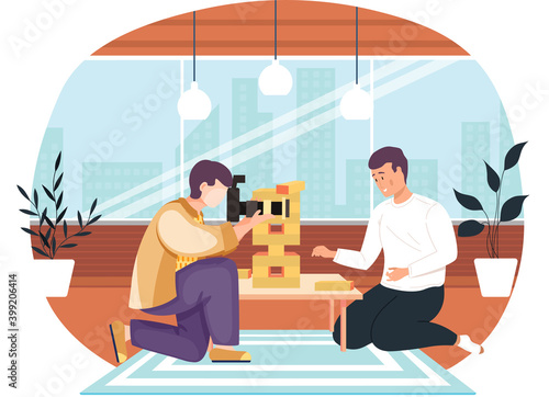 Man has fun with Jenga Tower on the table and on the blue carpet. Male character is playing board game. Table with folders and documents. The photographer takes pictures of the guy playing