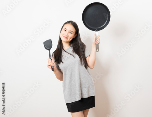 Young Asian woman with ladle and a pan on white background.