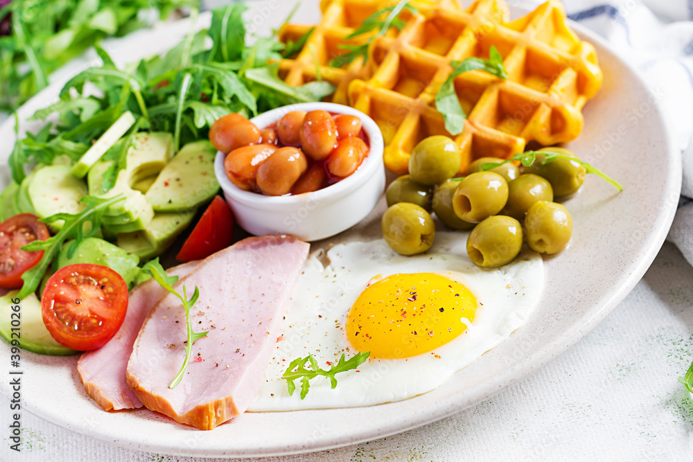 Breakfast with pumpkin waffles, fried egg, ham, tomato, avocado, beans and olives on white background. Appetizers, snack, brunch. Healthy food. Breakfast with pumpkin waffles, fried egg, ham, tomato, avocado, beans and olives on white background. Appetizers, snack, brunch. Healthy food.