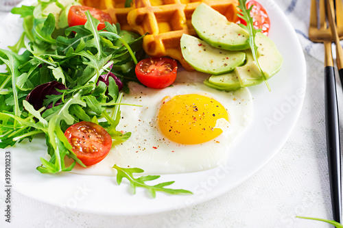 Breakfast with pumpkin waffles, fried egg, tomato, avocado and arugula on white background. Appetizers, snack, brunch. Healthy vegetarian food.