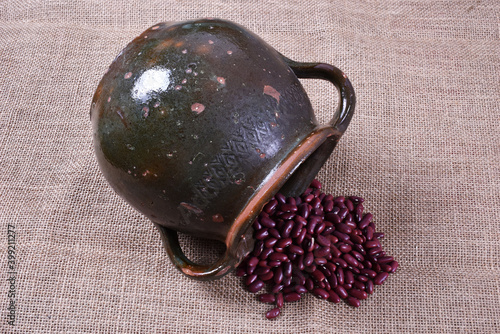 Red beans and old pot scattered on burlap background