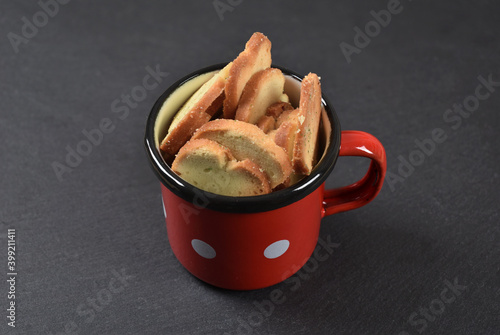 Red metal bowl with small bread snacks pieces on black background