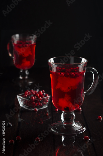 Red fruit tea with cowberry, blueberry in two transparent glasses on black wood table in dark interior, vertical.