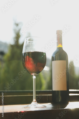 Glass and bottle of red wine on wooden windowsill against mountain background