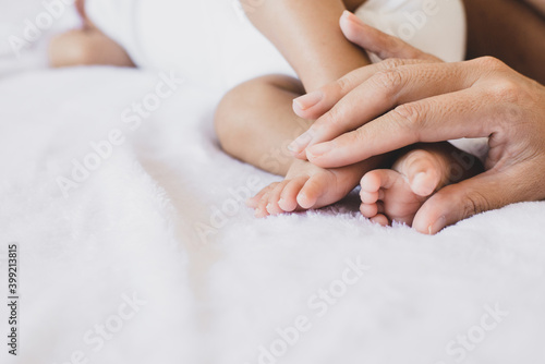 Mother hands holding baby feet lying on a comfortable bed at home Family concept
