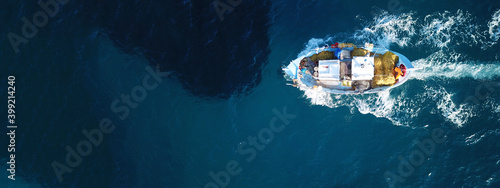 Aerial drone ultra wide photo of traditional wooden fishing boat with fishermen cruising Aegean deep blue sea, Cyclades, Greece