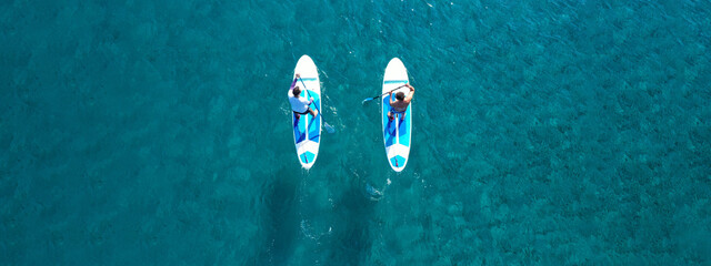 Aerial drone ultra wide photo of 2 men exercising sup board or Stand Up Paddle board in turquoise tropical clear bay
