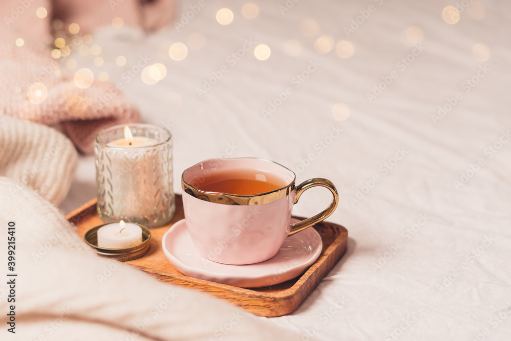 Fototapeta premium Details of still life in the home interior of living room. Sweater, cup of tea, cotton, cozy, book, candle. Moody. Cosy autumn winter concept. Decoration, vintage with glow bokeh.