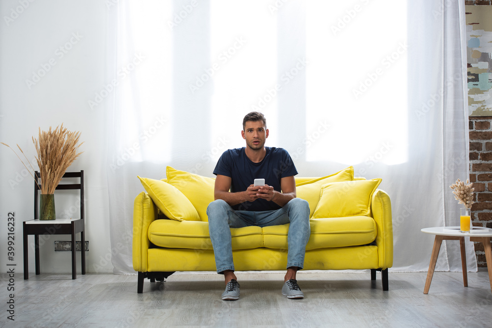  man holding smartphone while looking at camera on couch