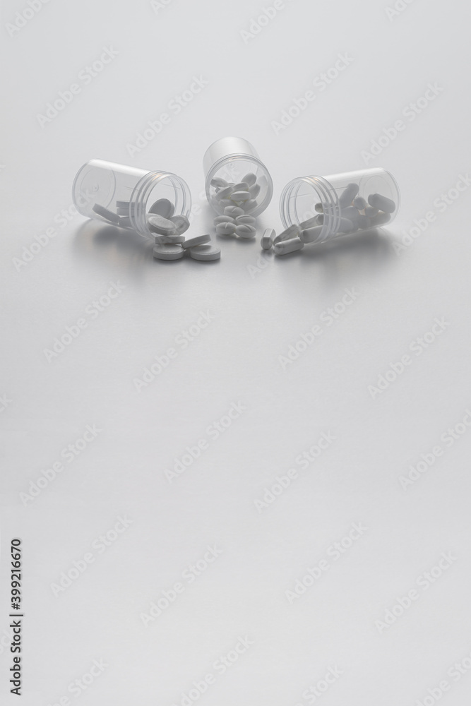 Three open transparent pill bottles with some pills on a white background. Three open transparent pill bottles with some pills on a white background.