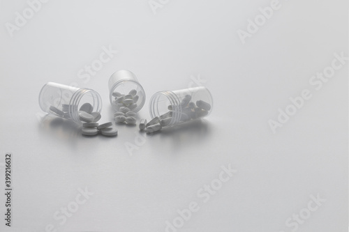Three open transparent pill bottles with some pills on a white background.