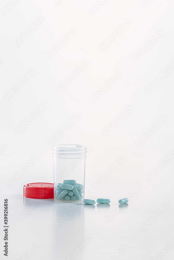 open transparent pill bottle with some pills outside and red caps on the white ground open transparent pill bottle with some pills outside and red caps on the white ground