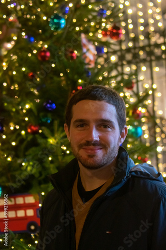 Photo of a young and attractive man smiling next to a Christmas tree at night full of beautiful lights. Christmas decorations. ornaments