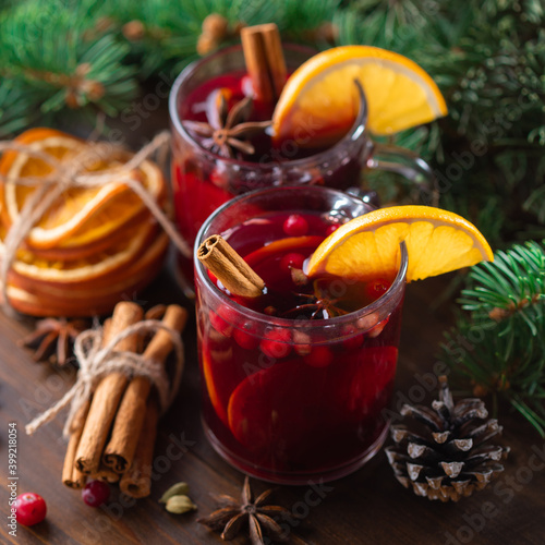 Fragrant, hot punch or mulled wine for Christmas in a glass on a wooden board and branches of a Christmas tree on the background. Hot winter drink of wine with spices and fruit.