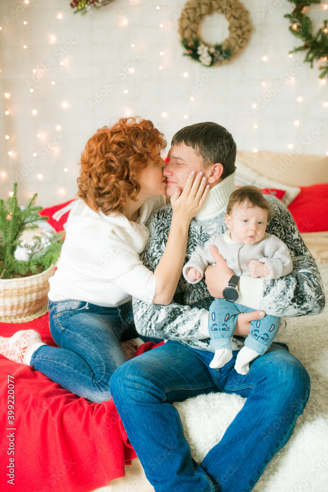 A young family in warm sweaters with a baby daughter in a Christmas bedroom interior decorated with red blankets, pillows, garlands and green pine needles. Family and Children. Christmas mood
A young family in warm sweaters with a baby daughter in a Christmas bedroom interior decorated with red blankets, pillows, garlands and green pine needles. Family and Children. Christmas mood