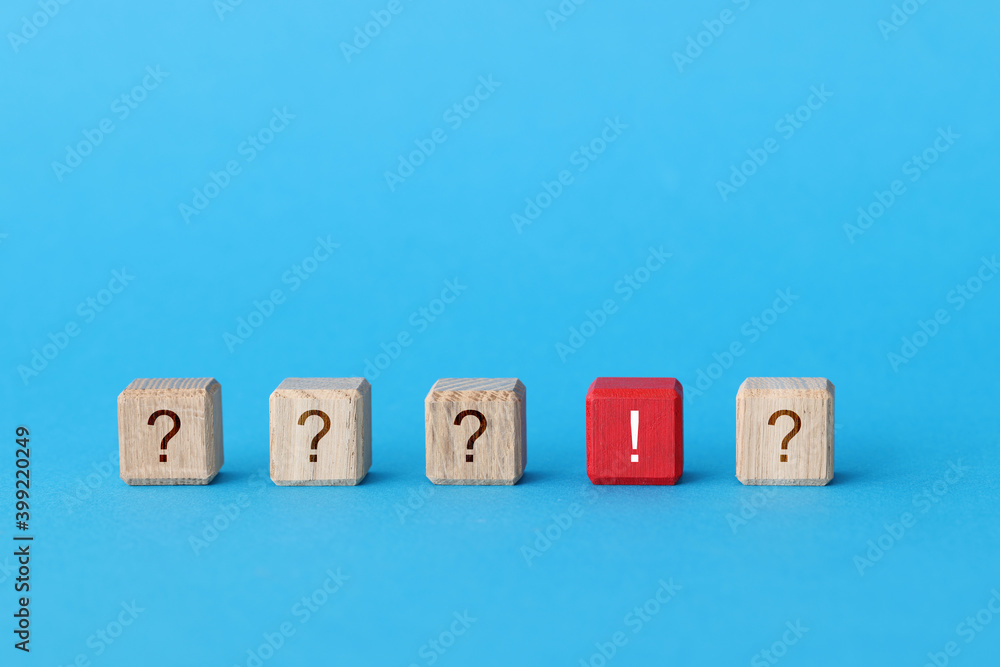 Red wooden cube with exclamation mark lying among cubes with question marks closeup Red wooden cube with exclamation mark lying among cubes with question marks closeup