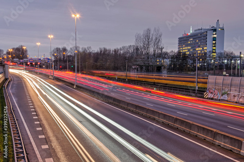 Rotterdam, The Netherlands, December 13, 2020: light trails of the car traffic on the A20 motorway, a passing yellow Dutch railways train and the St. Franciscus hospital in the blue hour