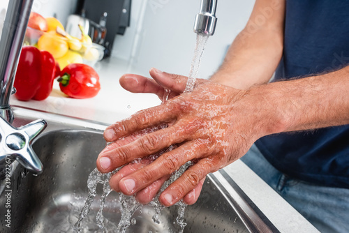 Cropped of man washing hands in kitchen near vegetables on blurred background