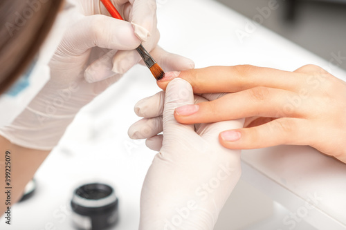 Manicure master is covering female nails with transparent nail polish in a nail salon