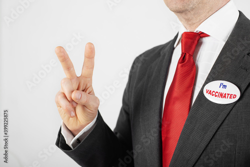 Middle age caucasian man in suit with button pin I'm vaccinated showing V gesture