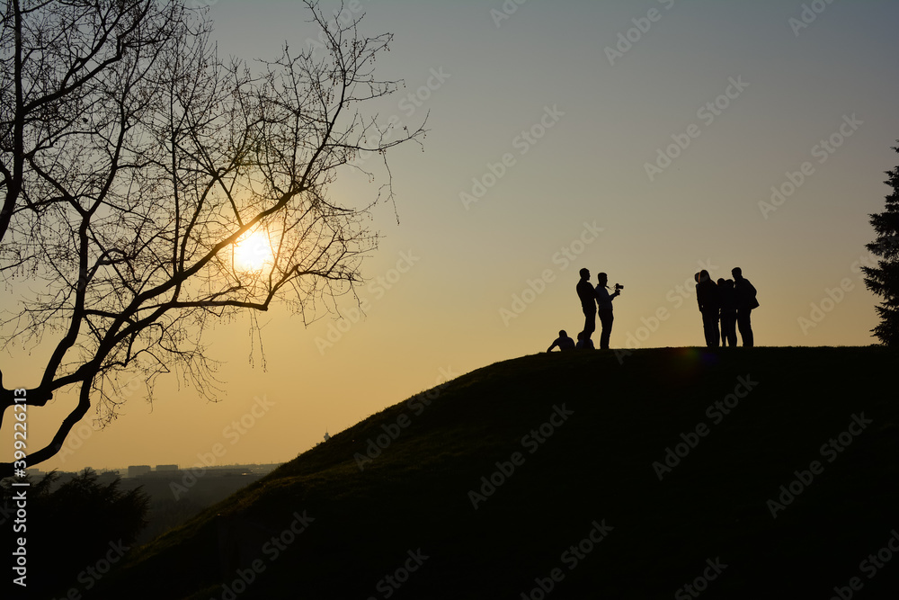 Silhouettes of people standing on top of the hill at colorful sunset doing a photoshoot with beautiful background of sun and monument  of Victory (Pobednik) on Kalemegdan, Belgrade, Serbia.
