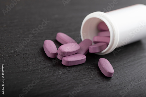 Pink pills are scattered from a white tube on a black background. Health care concept. Space for text.