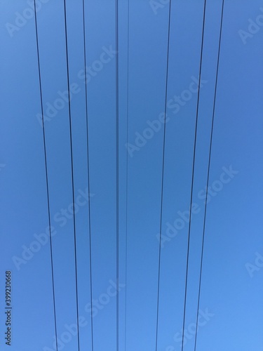 Thin black lines in the blue sky. Light blue sky. Straight lines of metal wires run against the blue sky. Wires at different heights.
