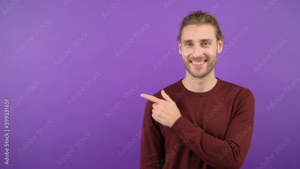 Half-length portrait of confident smiling funny young hipster man in burgundy sweater pointing to space on isolated purple background. 4K Half-length portrait of confident smiling funny young hipster man in burgundy sweater pointing to space on isolated purple background. 4K