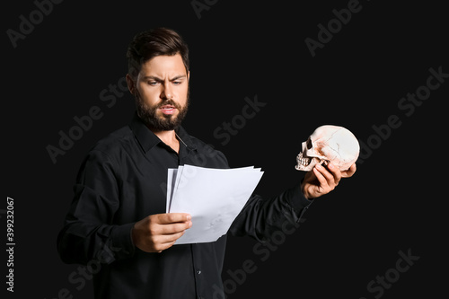 Male actor with human skull on dark background