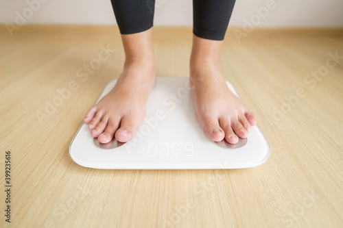 Woman standing on weigh electronic scalesfor check weight. diet lifestyle concept to reduce belly and weight control concept.