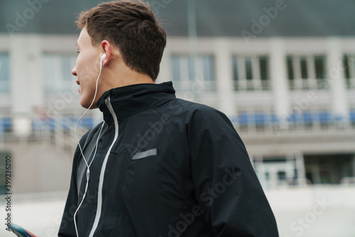 Handsome happy sportsman listening music with earphones and cellphone