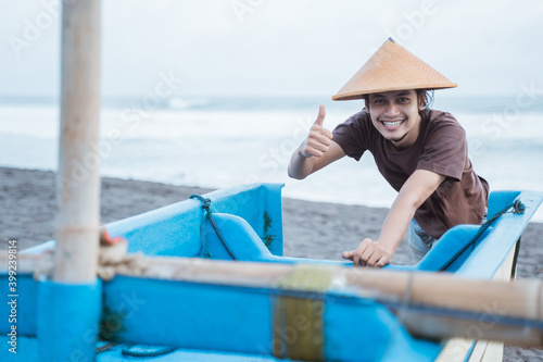 Portrait of a young fisherman pushing a boat showing thumbs after fishing