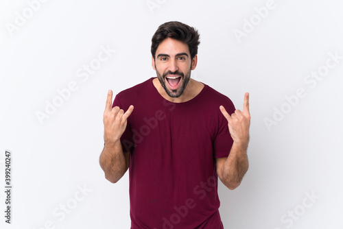 Young handsome man with beard over isolated white background making rock gesture © luismolinero