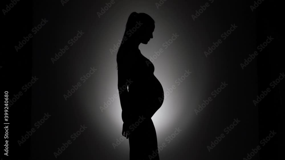 a silhouette of a pregnant woman entering the frame and caressing her belly on a black background a silhouette of a pregnant woman entering the frame and caressing her belly on a black background