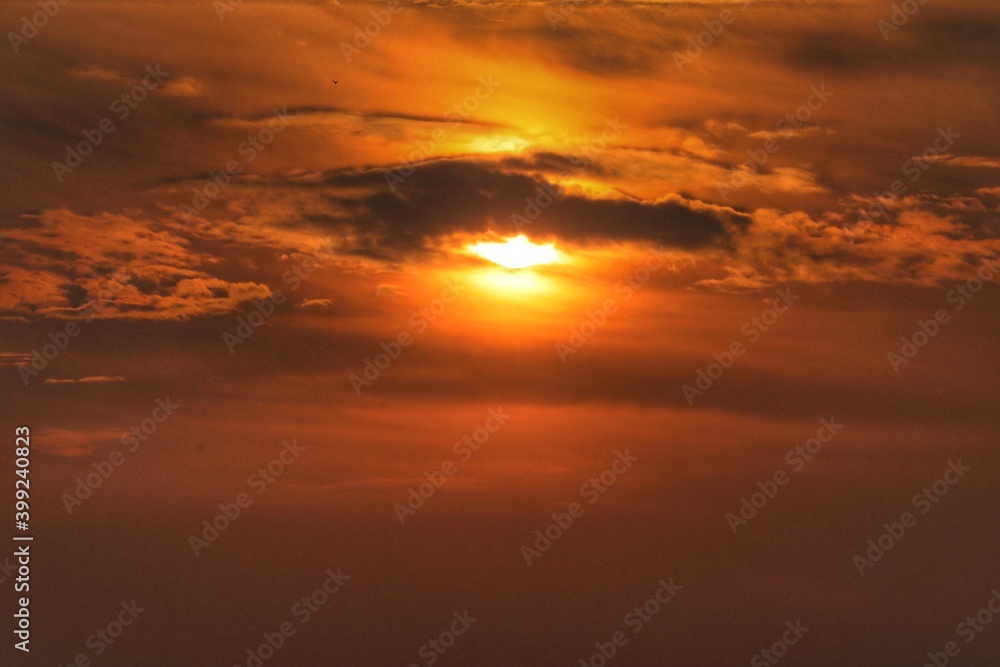 Sun hiding behind grey clouds with orange sky as background